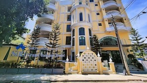 A multi-story hotel with a yellow facade, balconies, and a gated entrance. - Siri Ratchadamnoen Bangkok Hotel (Bangkok)