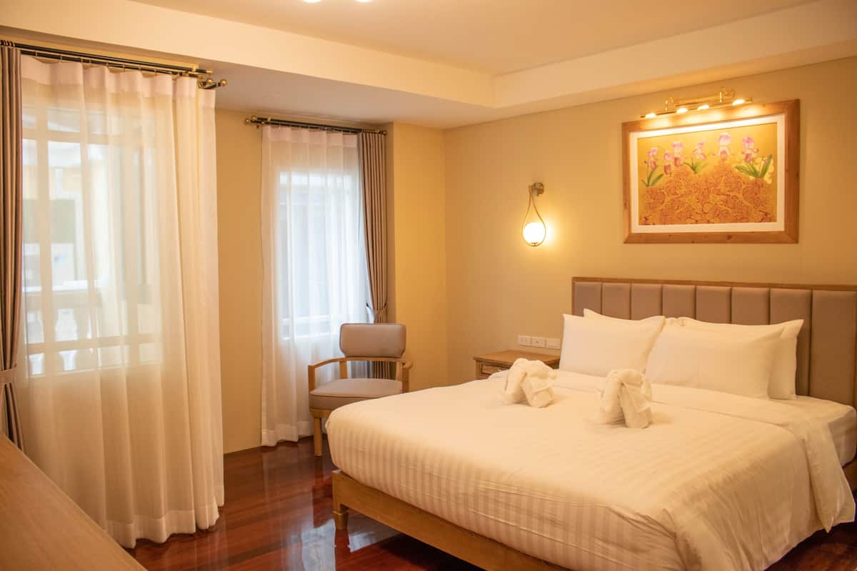 A hotel room with a large bed, a chair, a nightstand, and a wall-mounted light fixture.