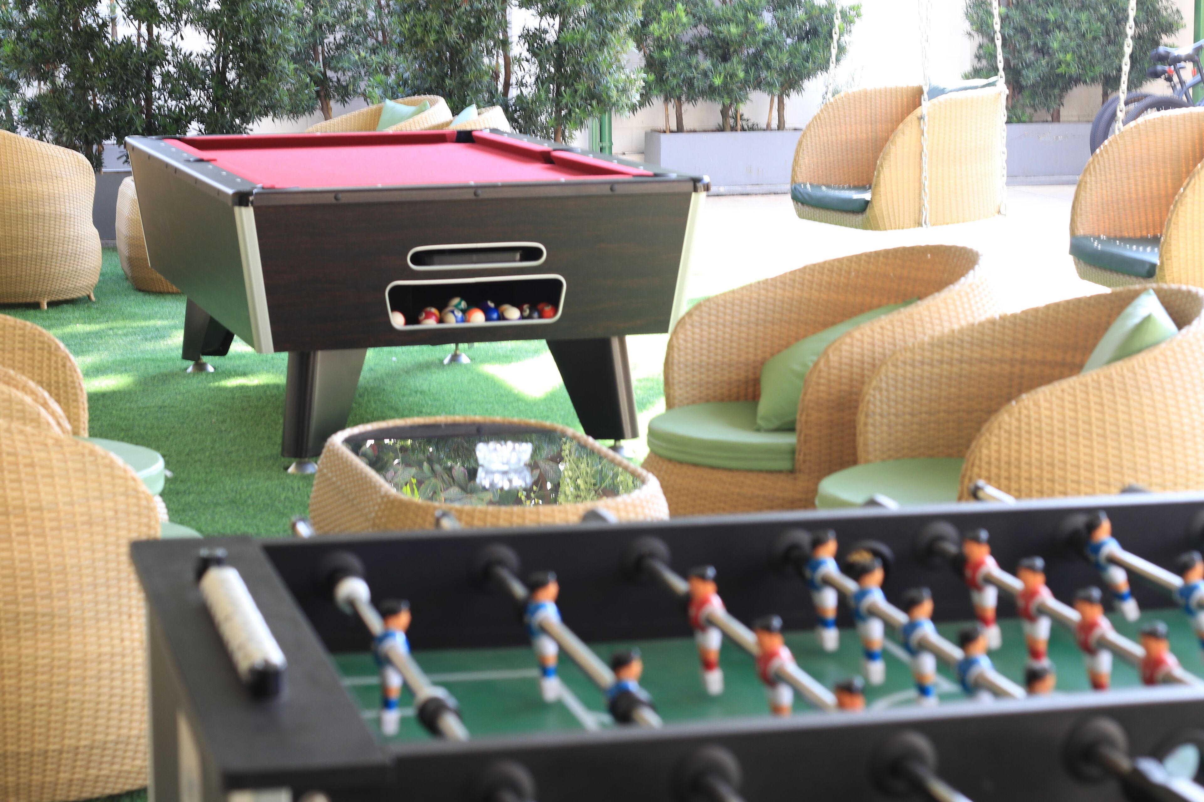 A pool table with a red felt surface, surrounded by wicker chairs with green cushions.