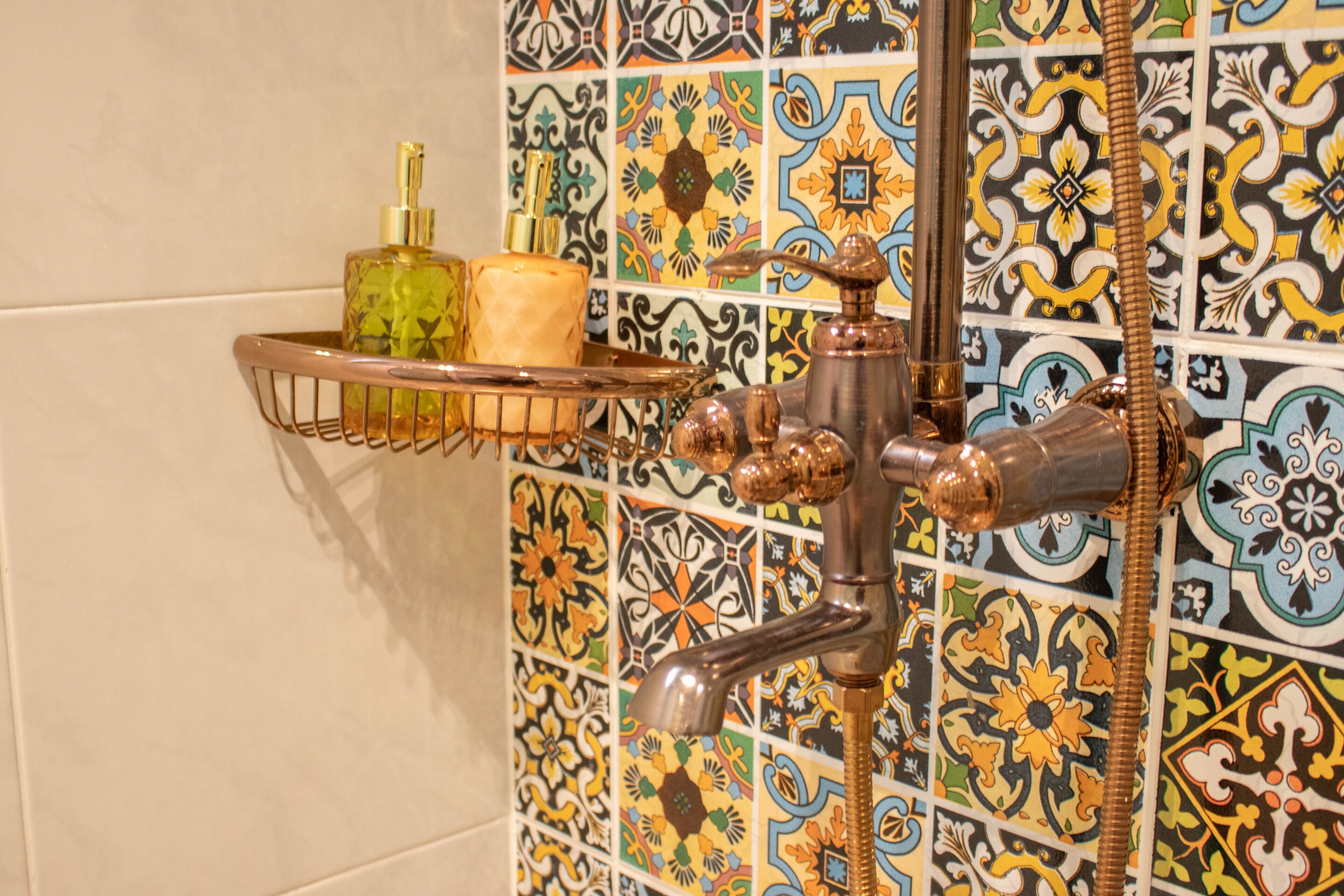 Un baño con pared de azulejos, ducha con cabezal de ducha manual y jabonera con botellas.