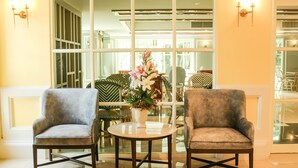 A seating area with two armchairs and a small table, a vase with flowers, and a large window with a view of the interior. - Siri Ratchadamnoen Bangkok Hotel (Bangkok)