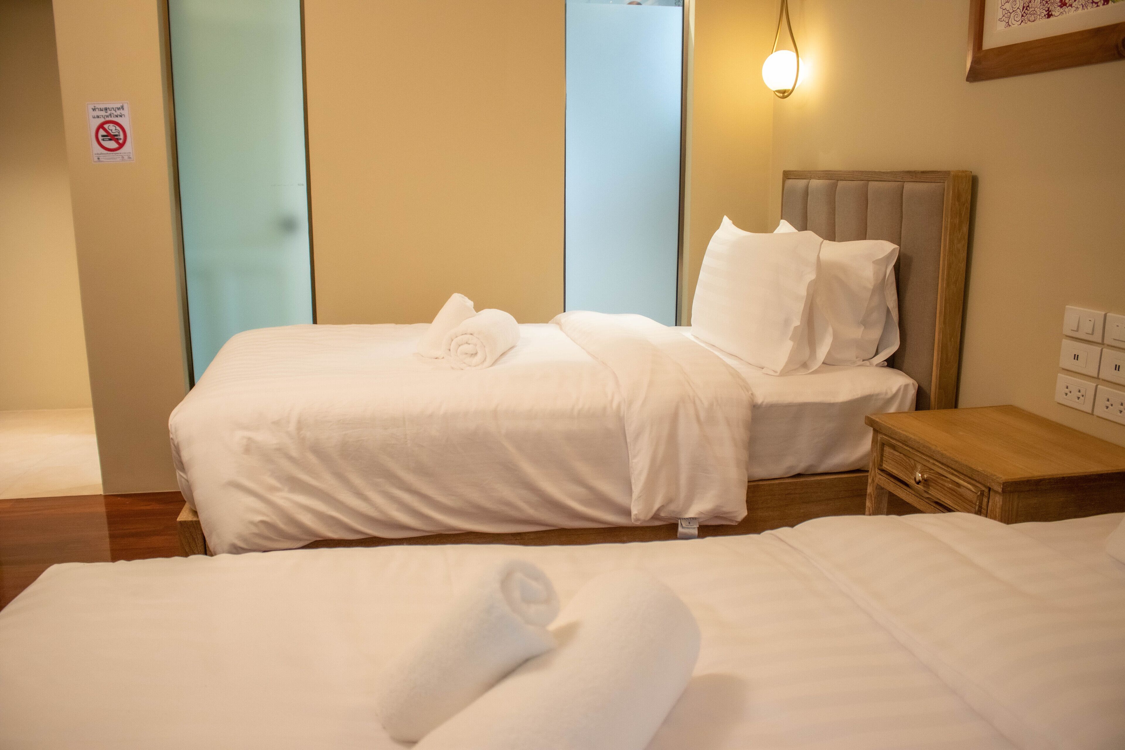 A hotel room with two beds, each with white linens and towels, a wooden nightstand, and a wall-mounted light fixture.