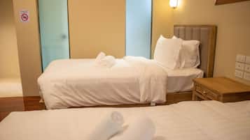 A hotel room with two beds, each with white linens and towels, a wooden nightstand, and a wall-mounted light fixture.