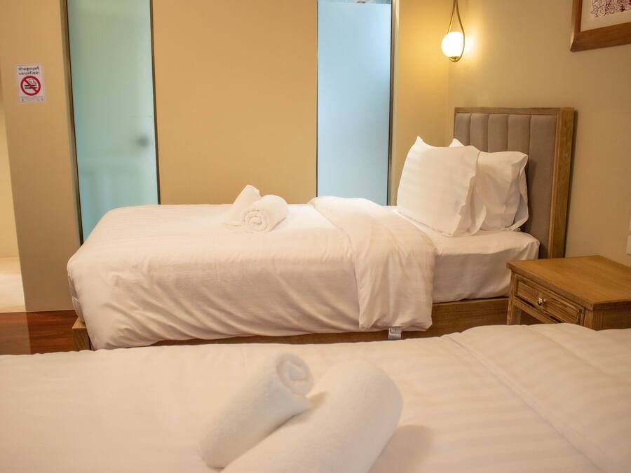 A hotel room with two beds, each with white linens and towels, a wooden nightstand, and a wall-mounted light fixture.