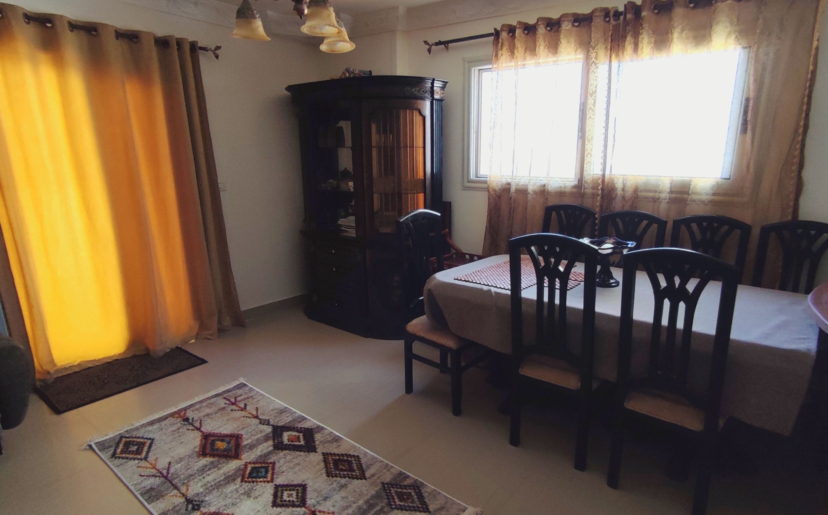 A dining area with a table and chairs, a wooden cabinet, and a window with curtains.