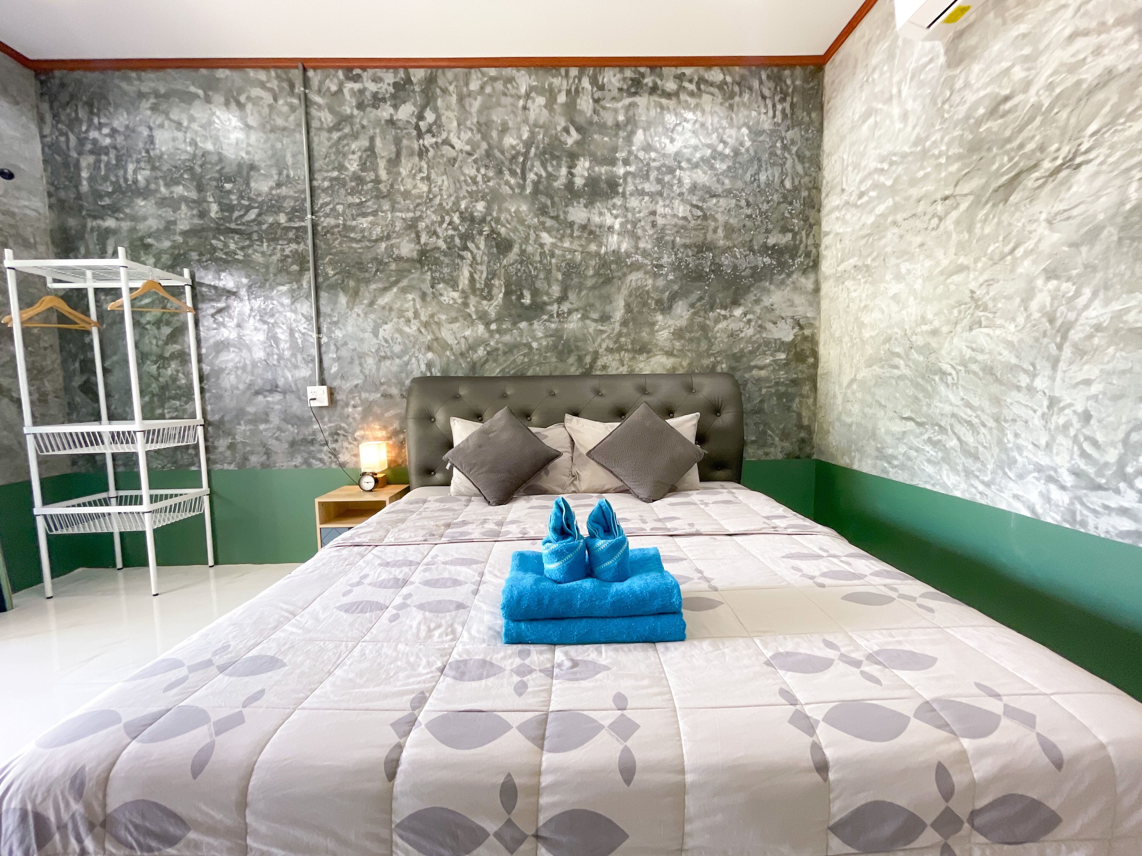 A bedroom with a bed, a nightstand, a wall-mounted shelf, and a hanging rack.