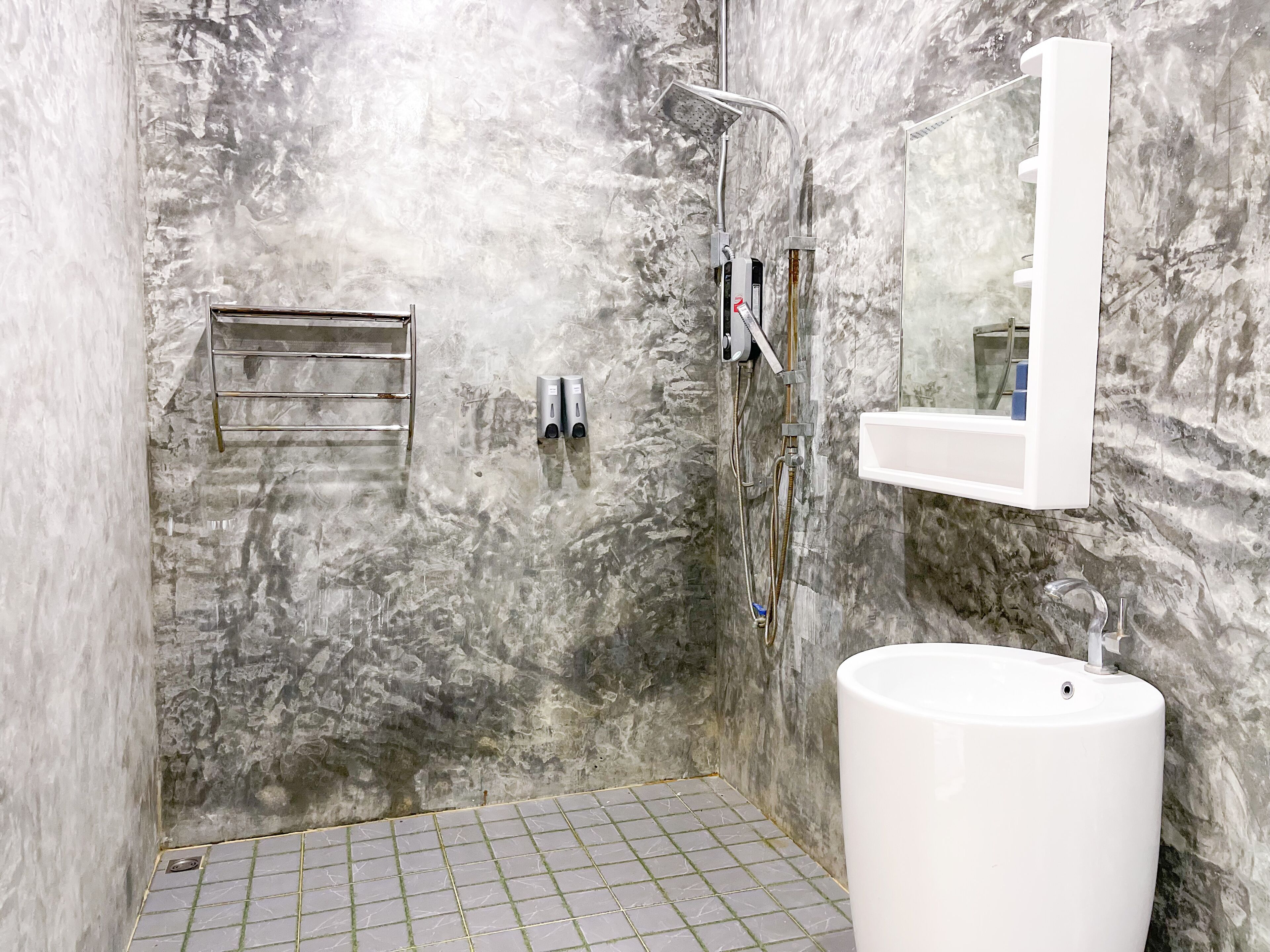 A bathroom with a marble wall, a shower, a sink, and a towel rack.