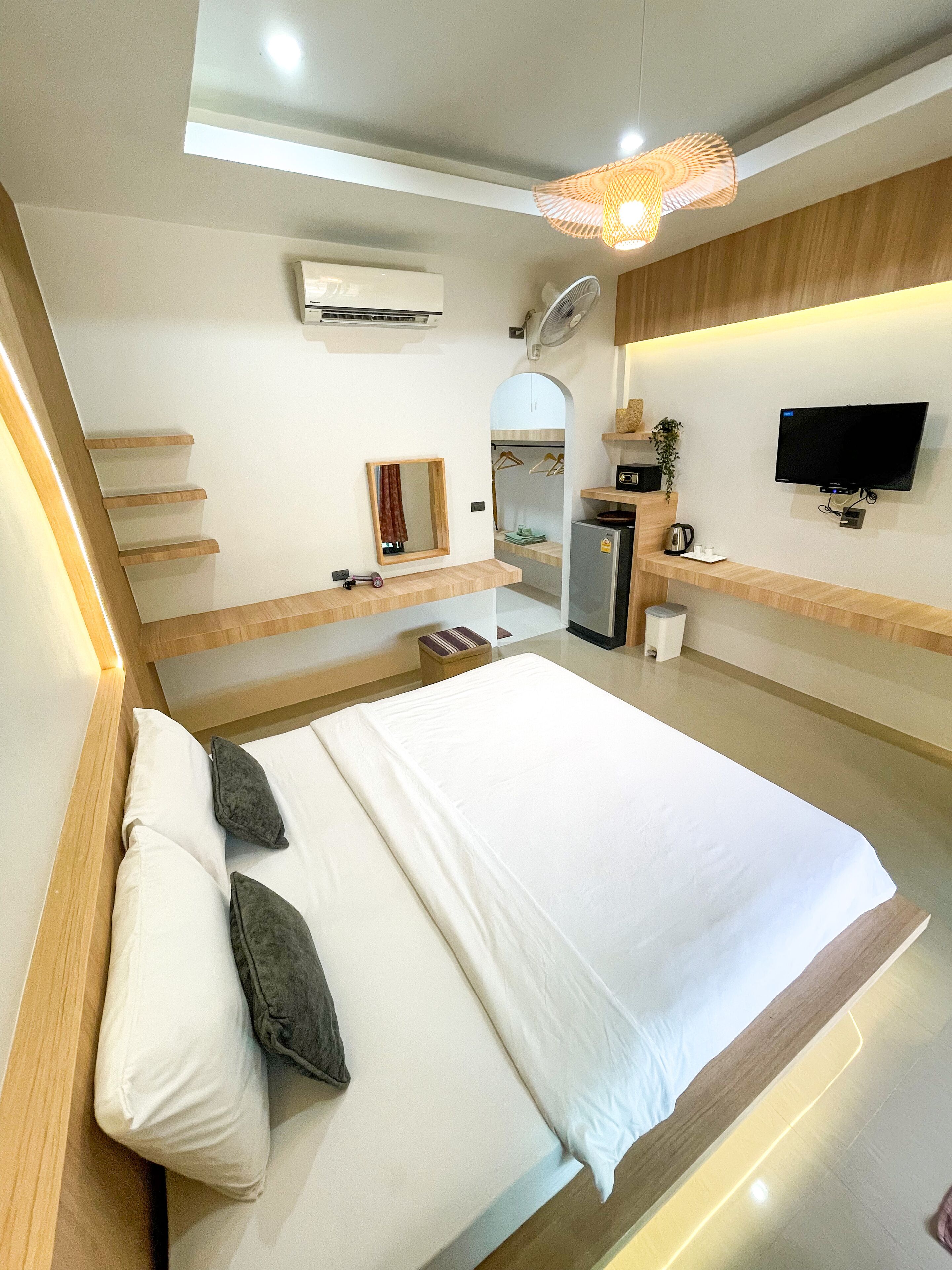 A modern hotel room with a large bed, a flat-screen TV, a desk with a chair, a mirror, and a small kitchenette.
