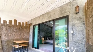 A modern room with a stone wall, a glass door leading to a balcony, a wooden table with benches, and a bed with a headboard. - Dara Homestay Koh Kood (Ko Kood)