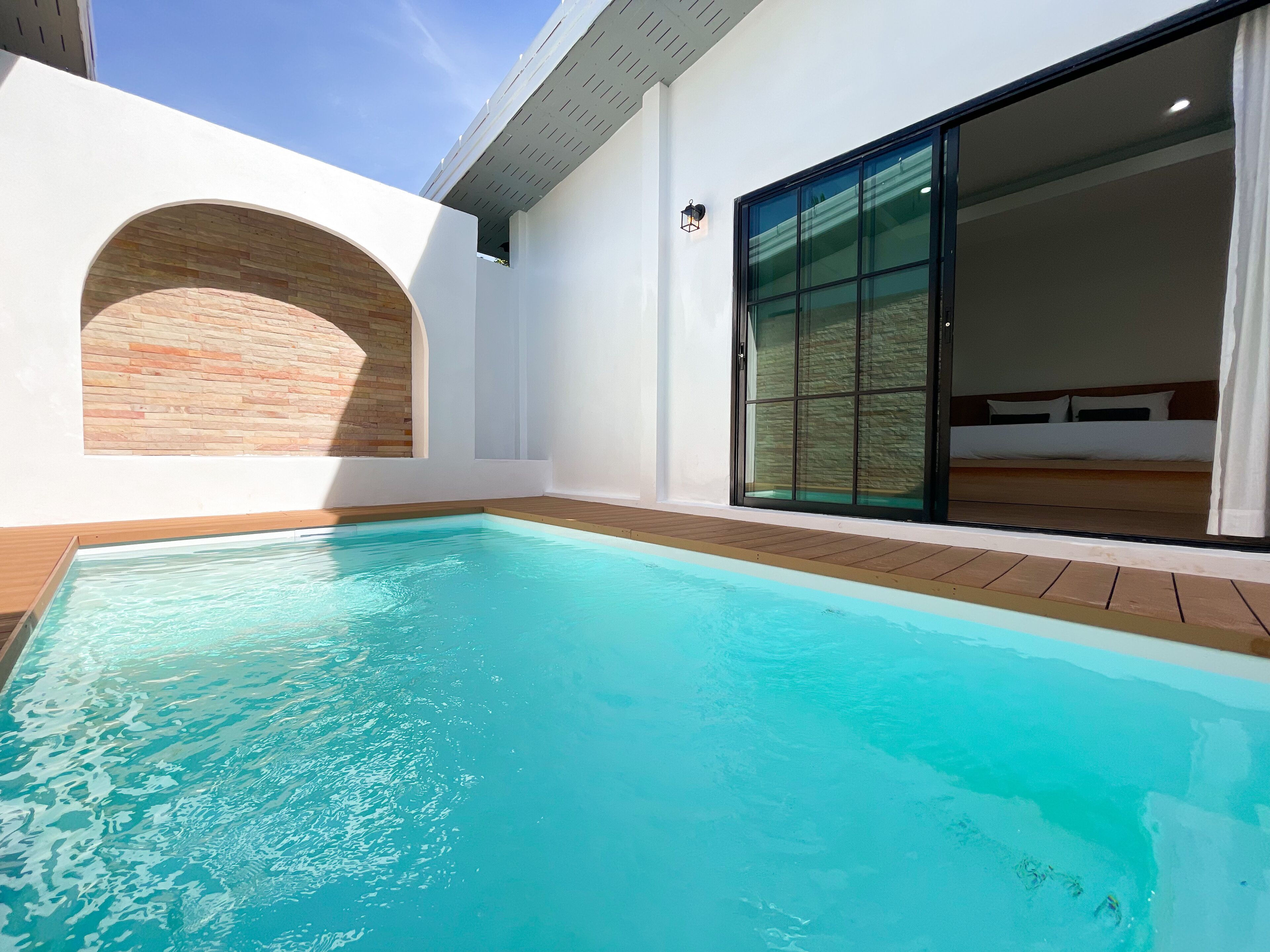 A modern hotel room with a large sliding glass door, a small pool, and a brick accent wall.