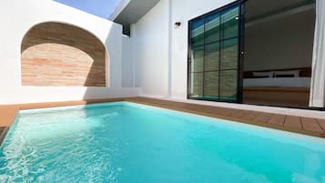A modern hotel room with a large sliding glass door, a small pool, and a brick accent wall.