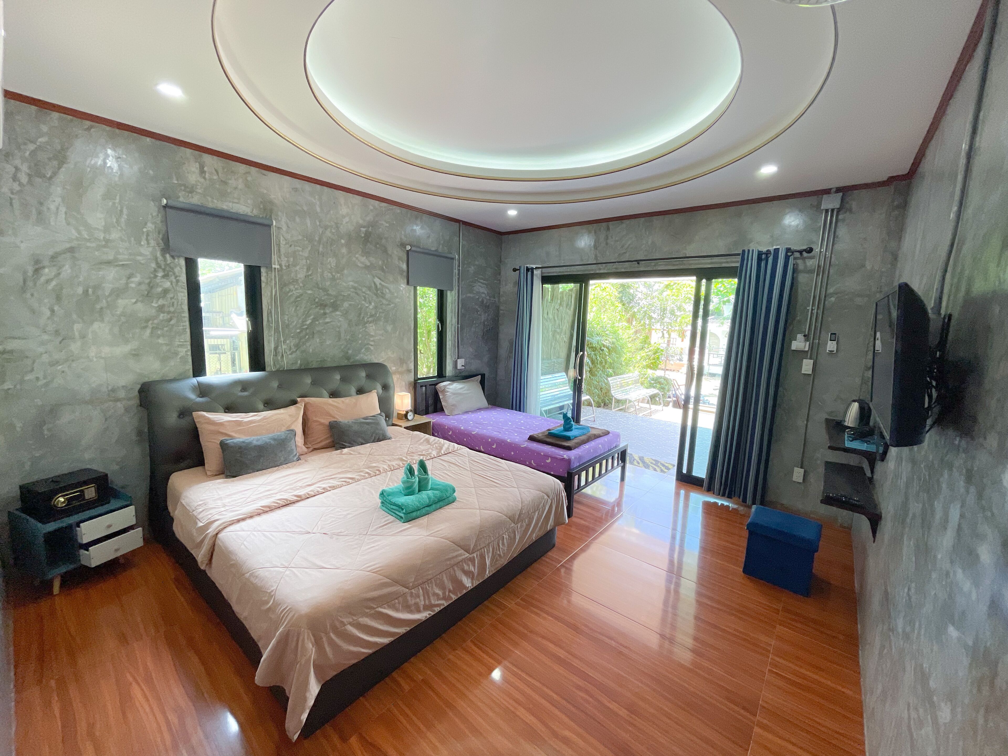 Un dormitorio moderno con una cama grande, una cama más pequeña, un televisor y un ventanal corredizo al exterior.