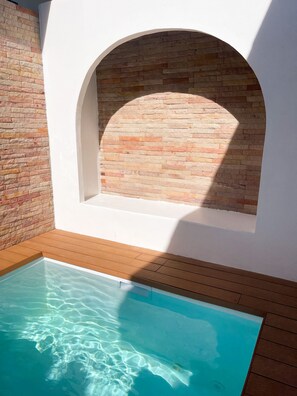 A swimming pool with clear water, surrounded by wooden decking and a brick wall with an arched window. - Dara Homestay Koh Kood (Ko Kood)