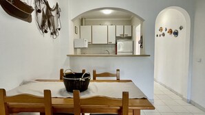 A dining area with a table, chairs, a basket, and a kitchen with cabinets and a microwave. - ESPLENDID 11 (Estartit)