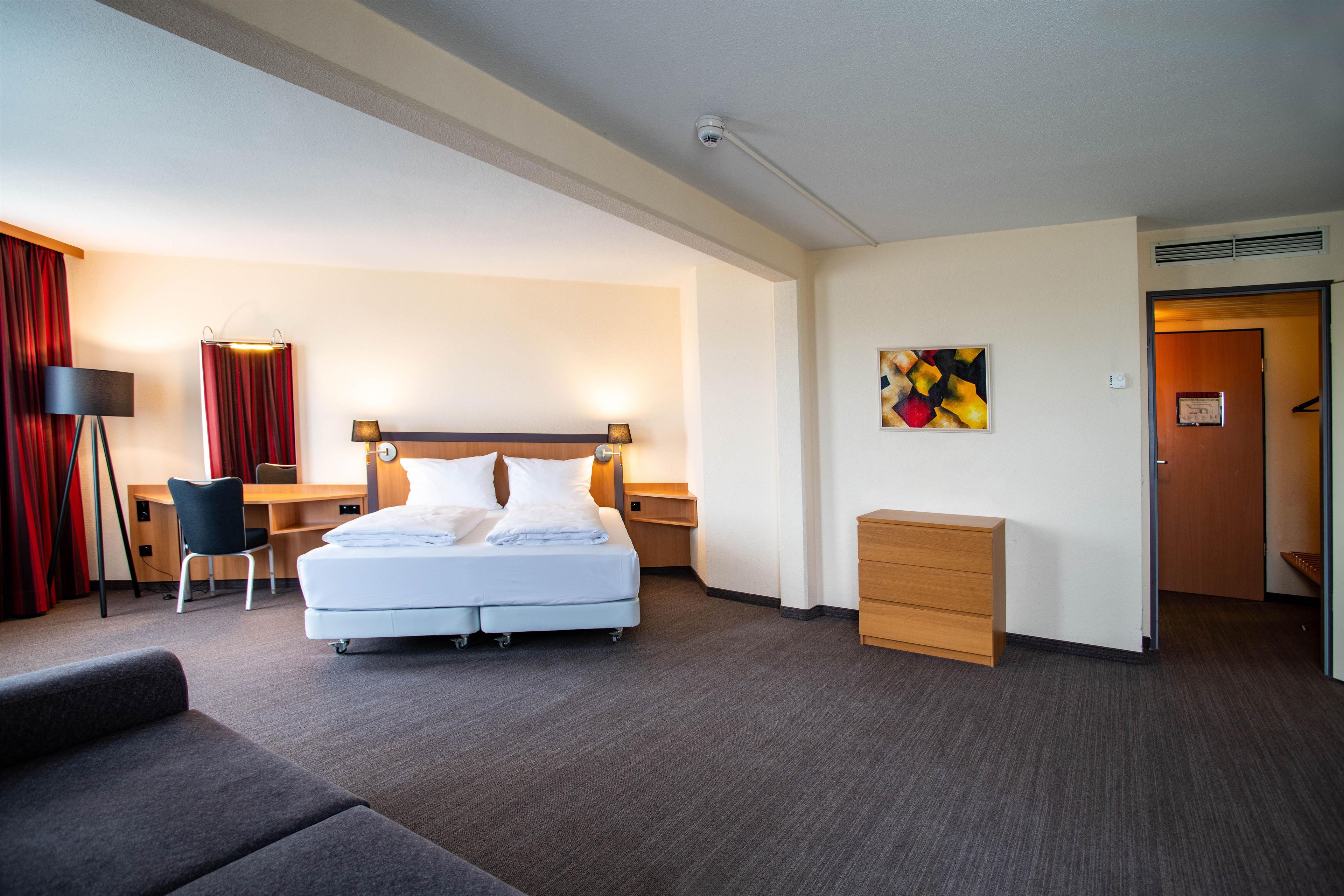 Una habitación de hotel con cama, escritorio, silla y una cómoda de madera pequeña.