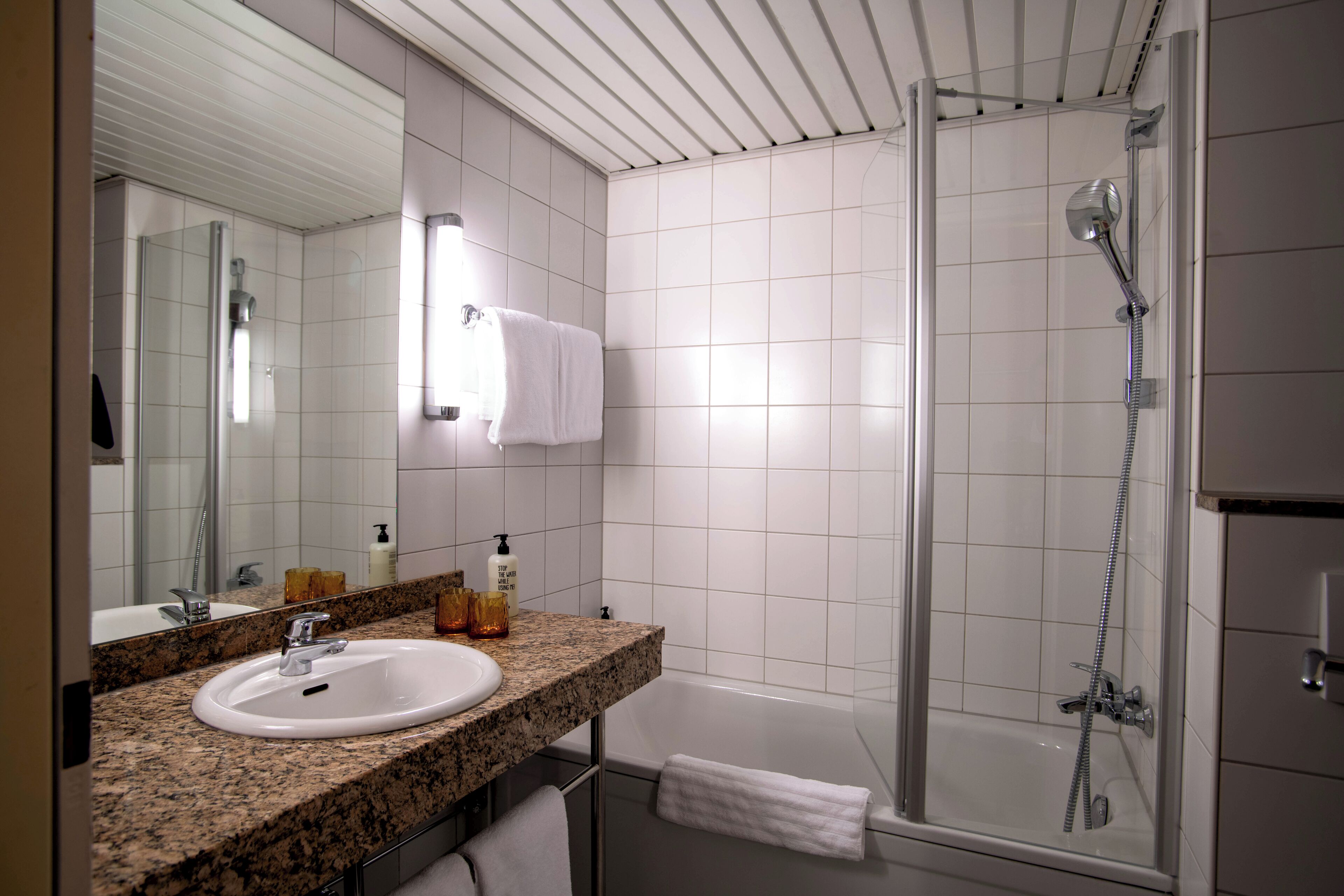 A modern bathroom with a granite countertop, white sink, and a glass-enclosed shower.
