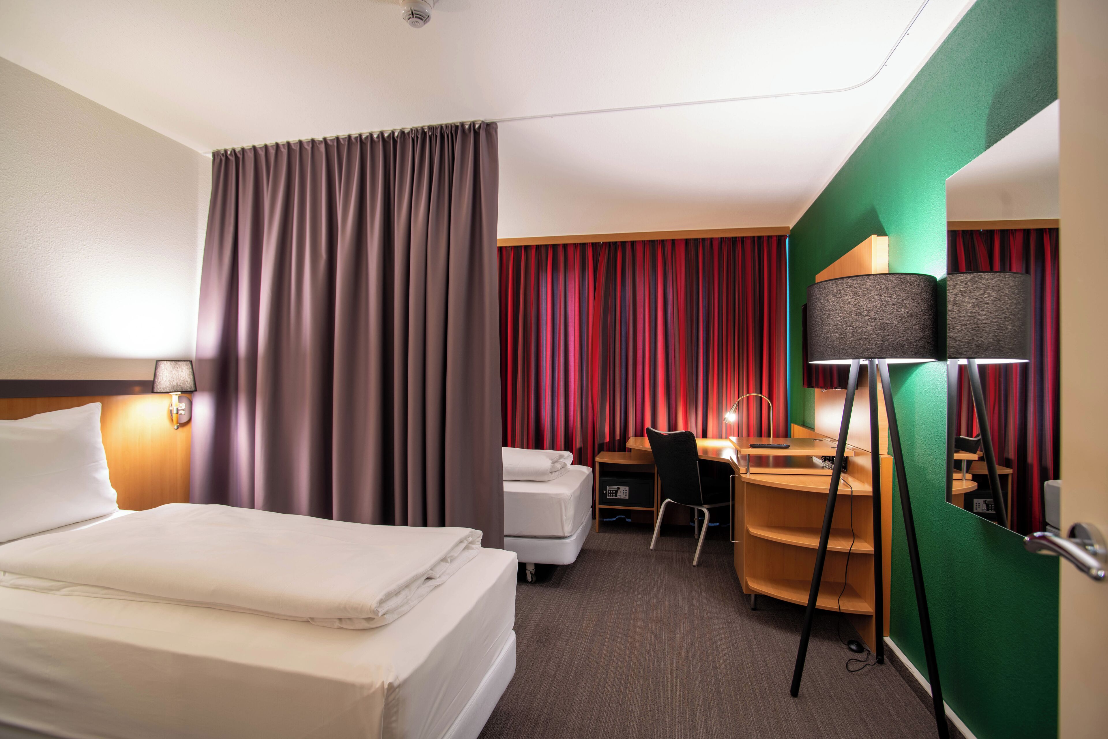 A hotel room with a bed, desk, chair, and curtains.