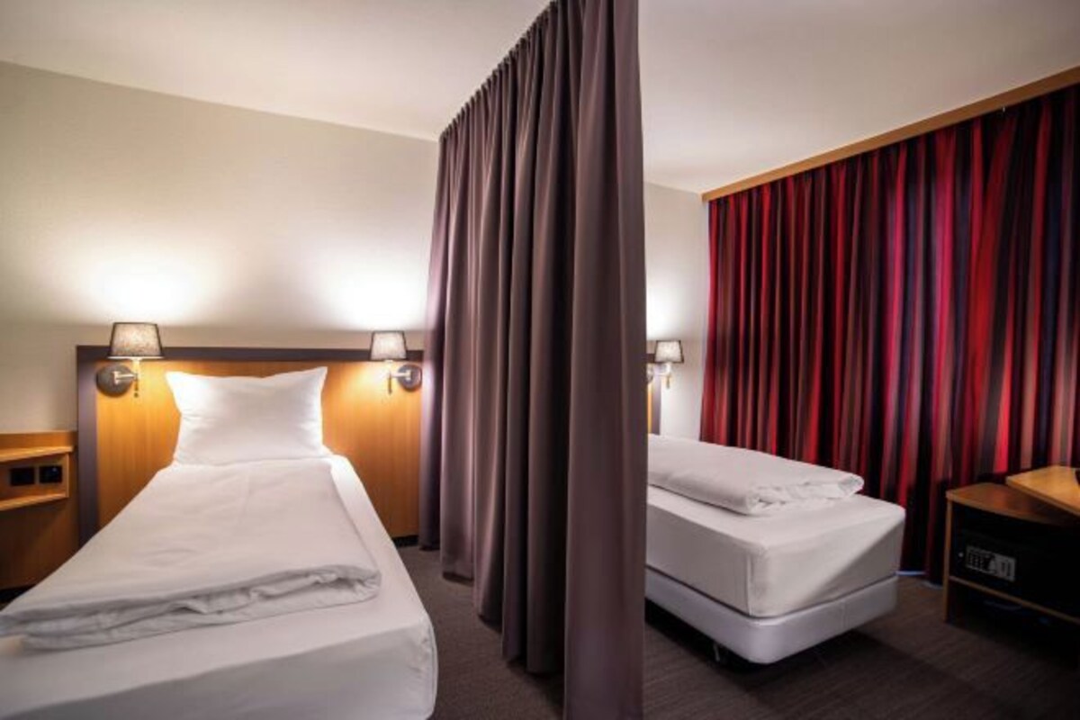 A hotel room with two beds, a curtain divider, and a red curtain on the right wall.