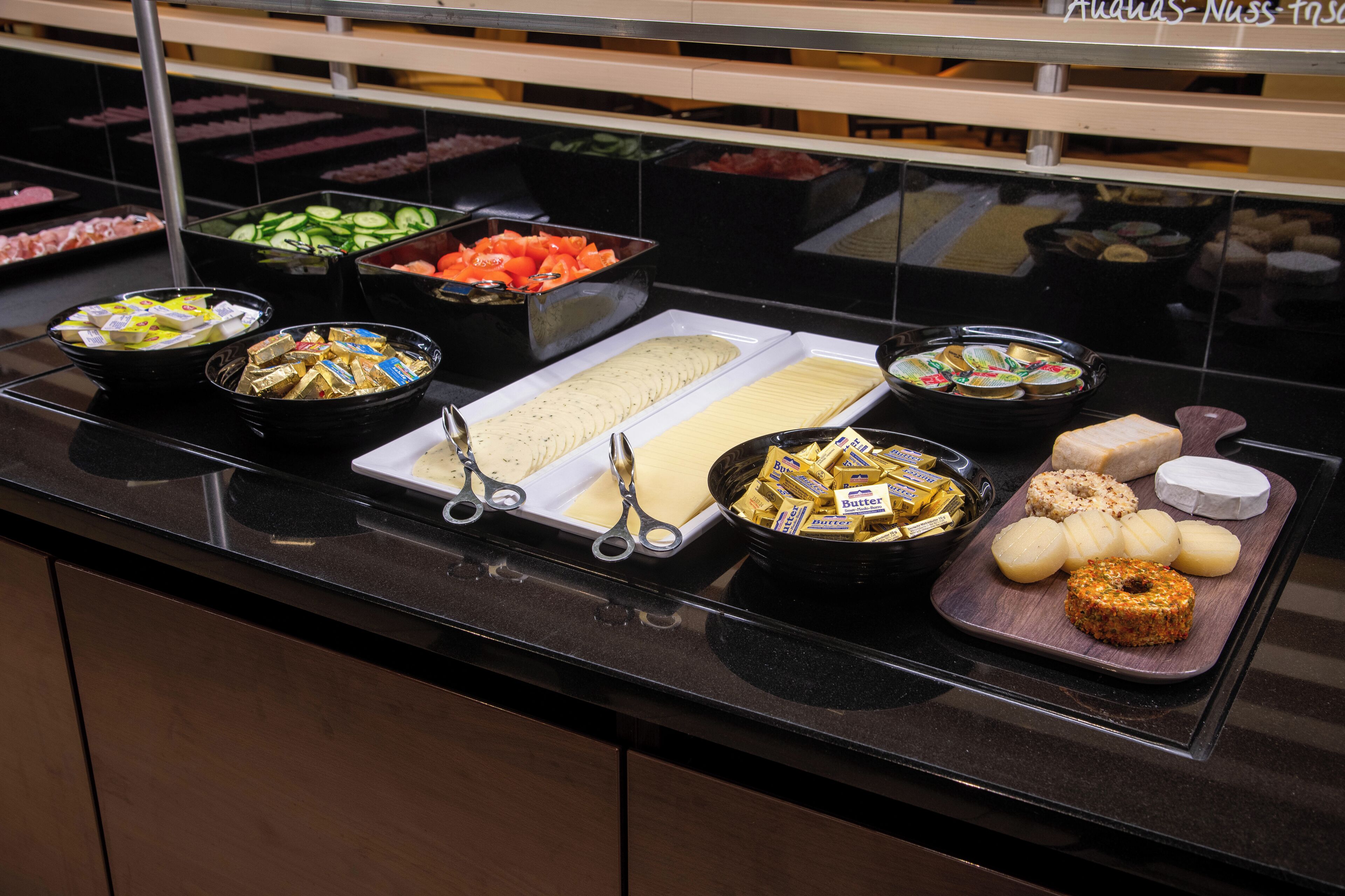 A buffet with various food items including sliced cucumbers, tomatoes, cheese, and butter.