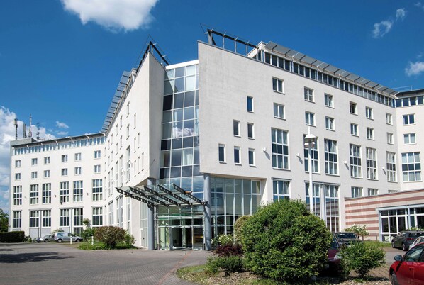 A modern building with a glass entrance, multiple windows, and a parking area with cars. - Best Western Conference Airporthotel Frankfurt Mörfelden (Moerfelden-Walldorf)