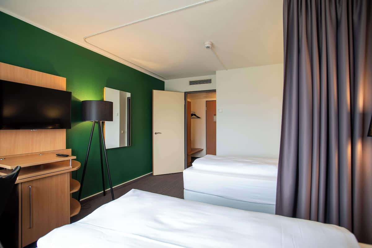 Une chambre d’hôtel avec deux lits, un bureau avec une chaise, un téléviseur à écran plat, une lampe et une armoire.