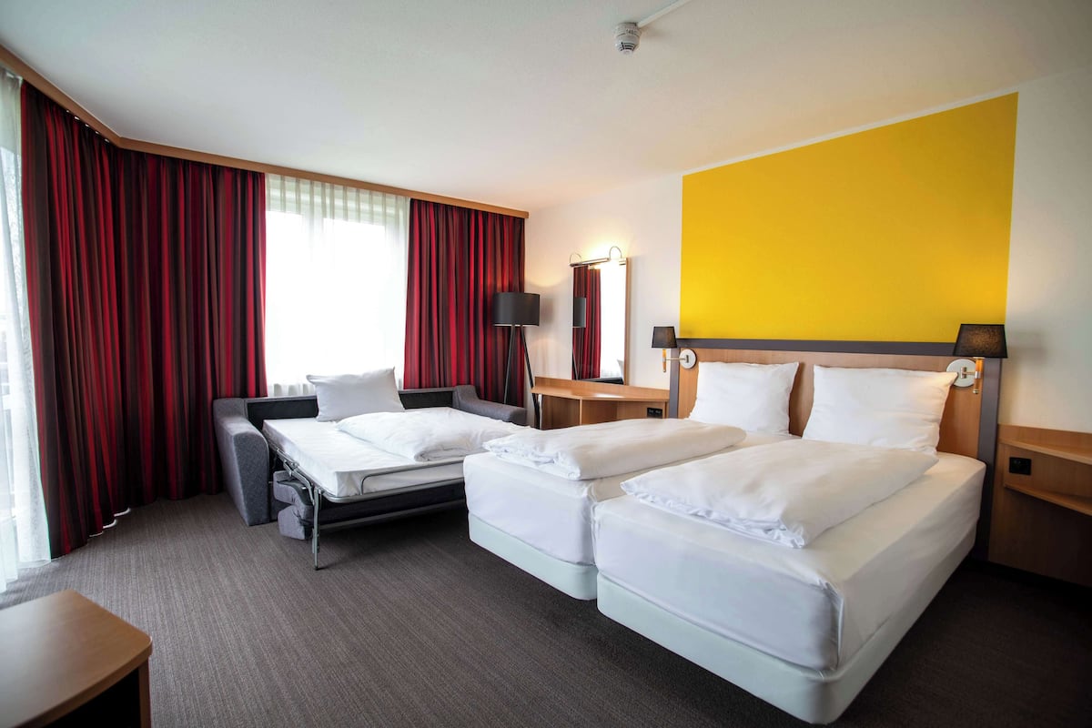 Une chambre d’hôtel avec deux lits, un bureau, une chaise, une lampe et un miroir.