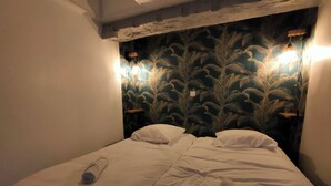 A bed with white linens and two pillows, a wooden headboard with a palm leaf pattern, and two wall-mounted lights.