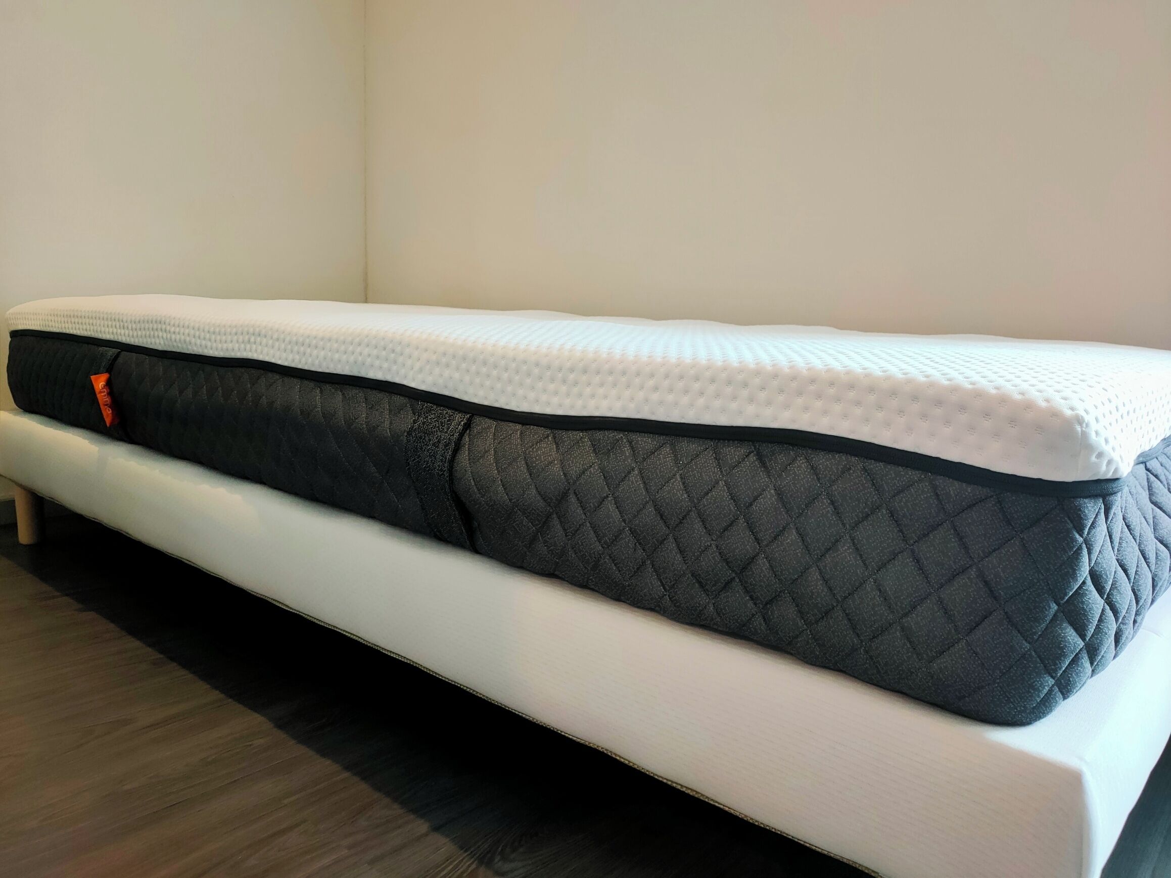 Un lit simple avec un matelas blanc et un surmatelas noir matelassé.
