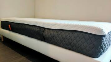 Un lit simple avec un matelas blanc et un surmatelas noir matelassé.