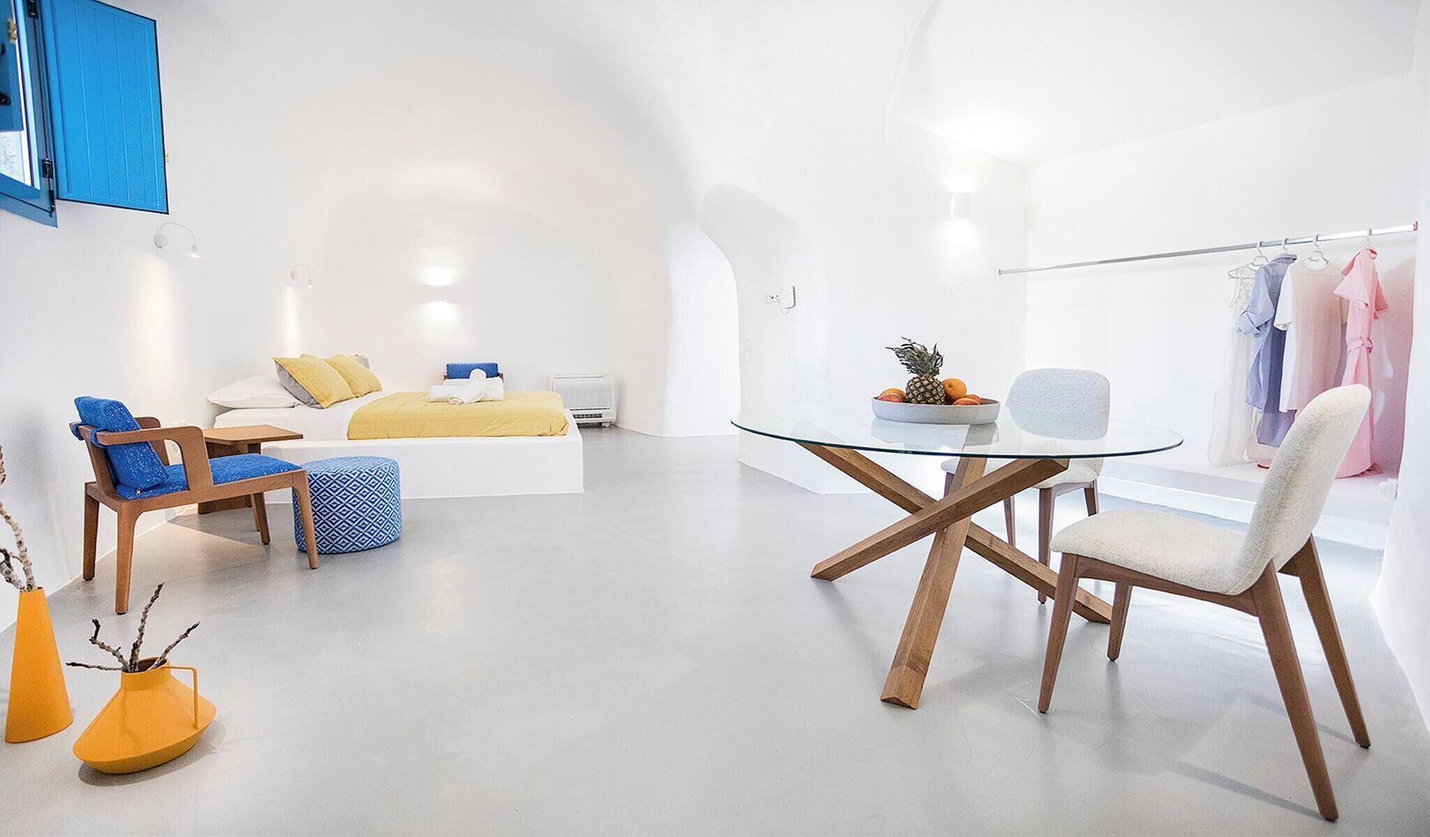 Ein modernes Hotelzimmer mit einem Bett, einer Sitzecke mit Stühlen, einem Glastisch und einem Kleiderständer.