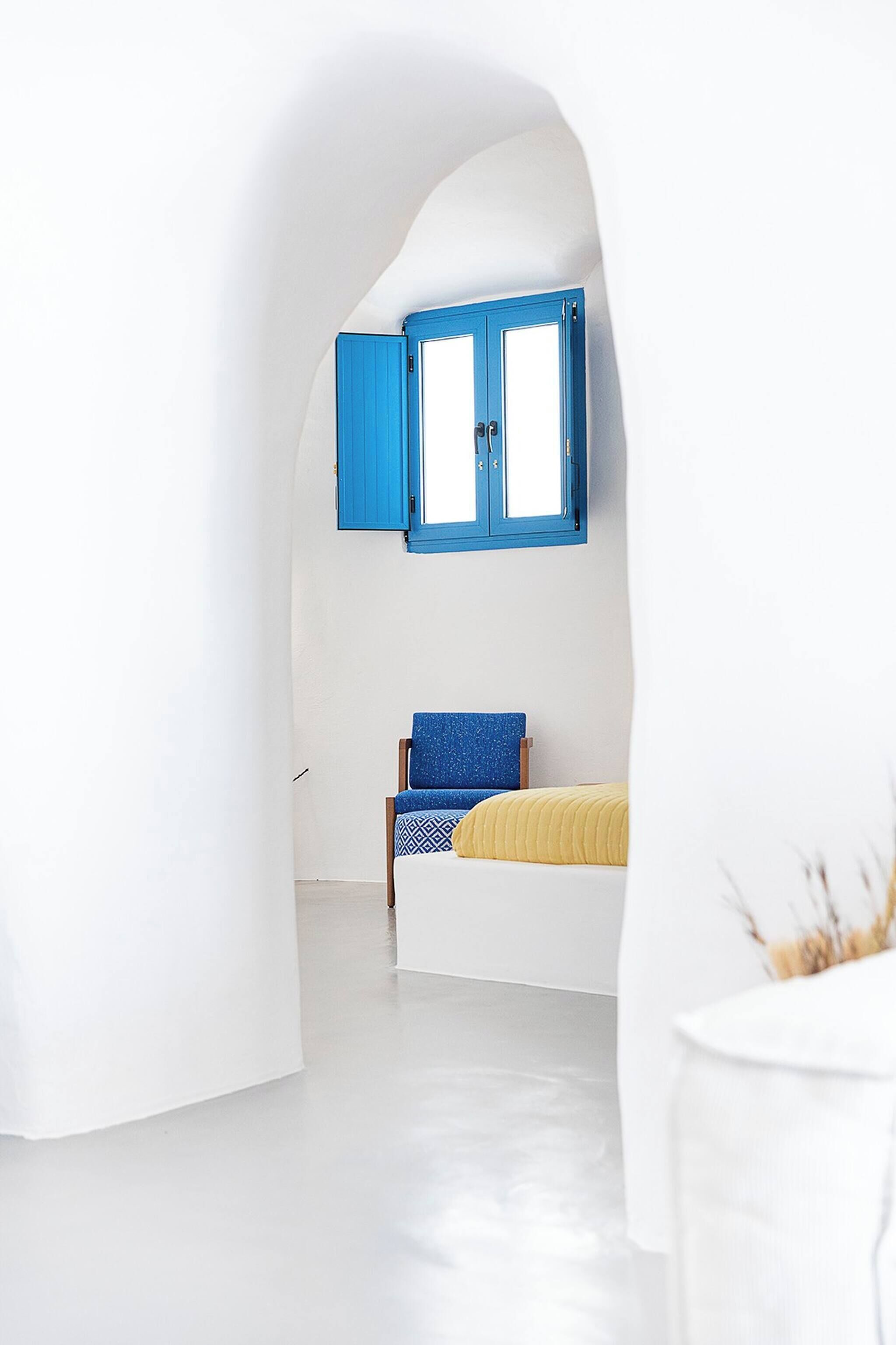 A room with a bed, a chair, and a window with blue shutters.