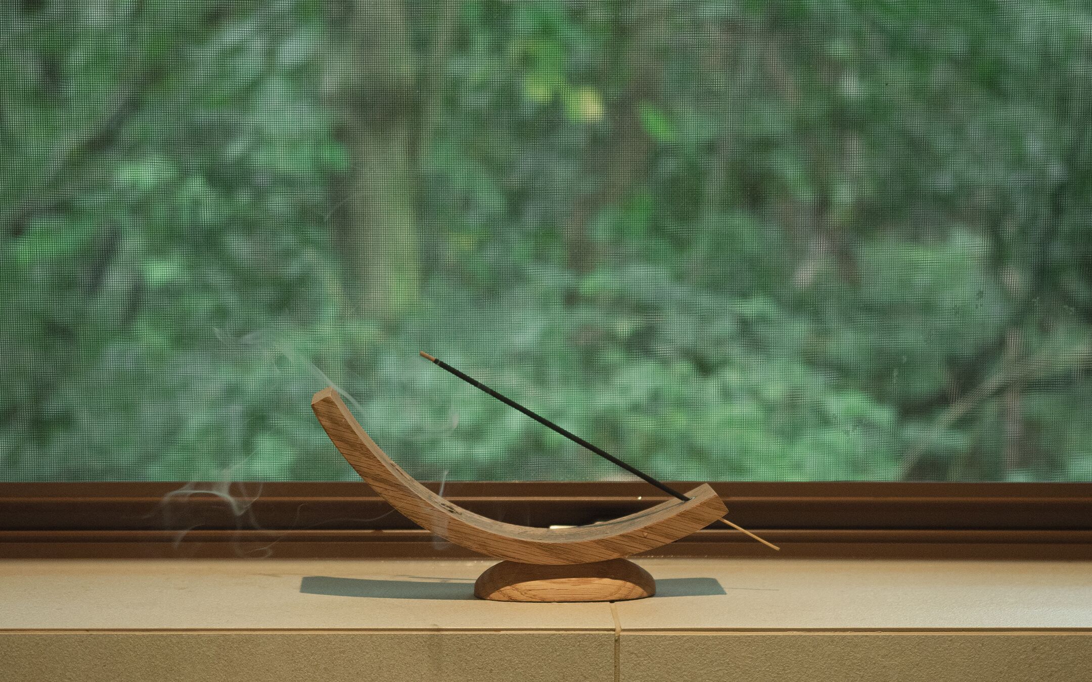 Ein traditioneller japanischer Räucherofen auf einem Holzständer, vor einem Fenster mit Blick auf einen grünen Wald platziert.