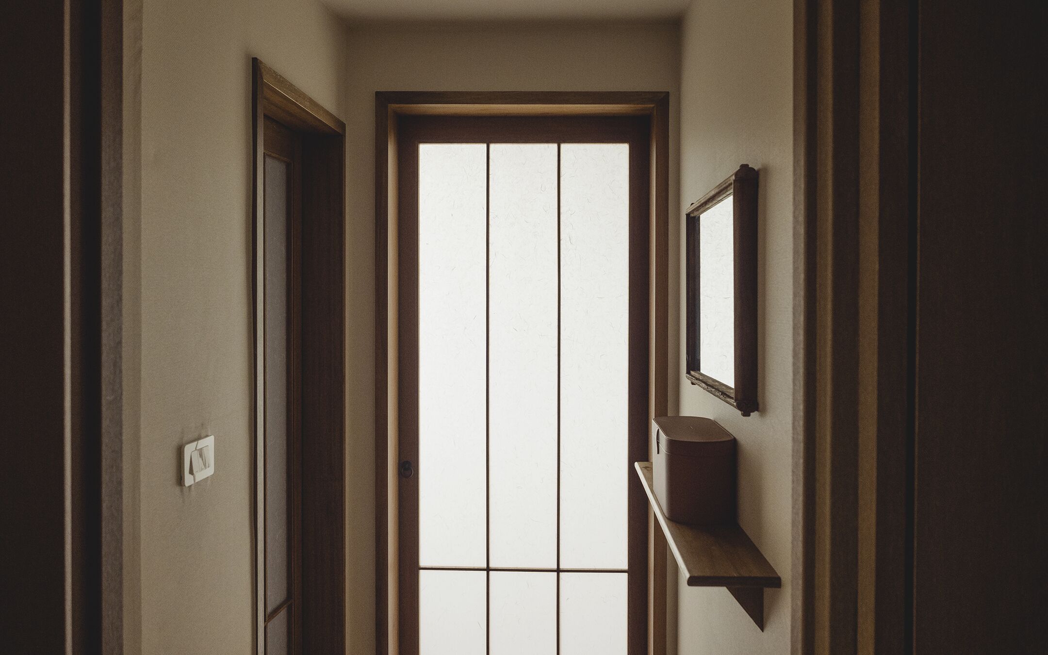 A hallway with a door, a window, and a shelf with a container.