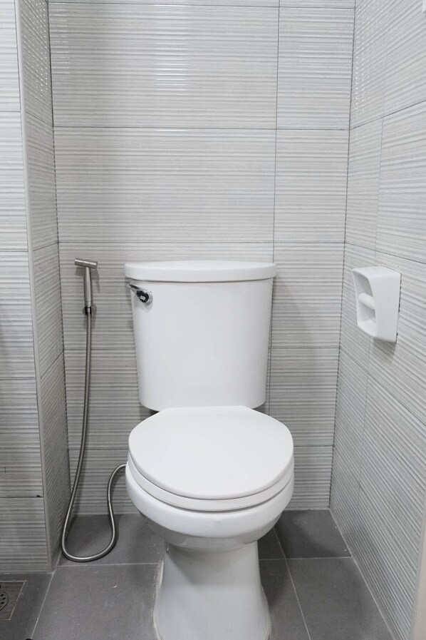 Une petite salle de bain moderne avec des toilettes blanches, une douchette à main et un distributeur de savon fixé au mur.