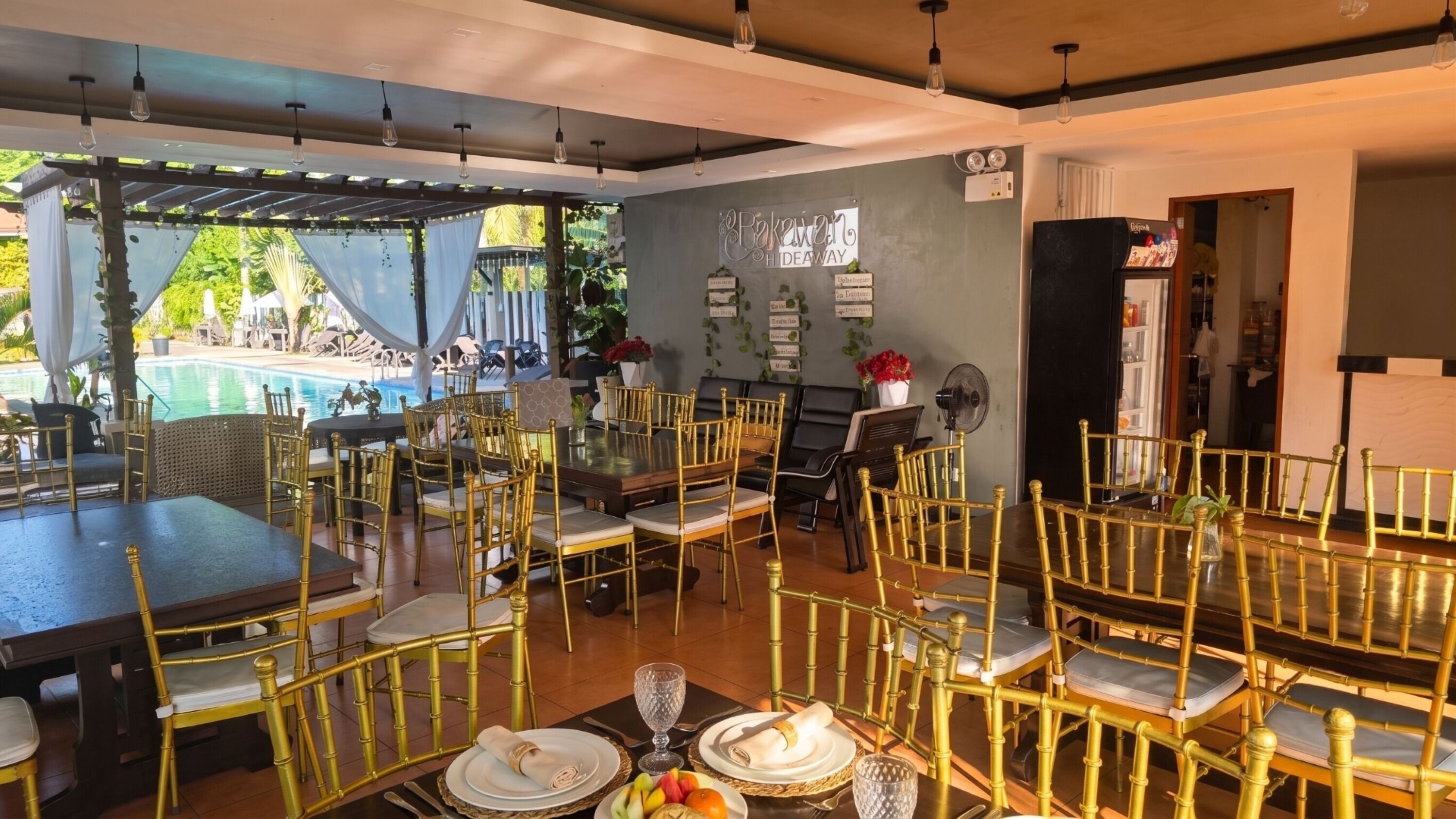 A dining area with tables and chairs, a pool view, and a sign reading 'Bakery Hideaway'.