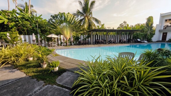 Un área de piscina con sillones de descanso, una pérgola y plantas tropicales.