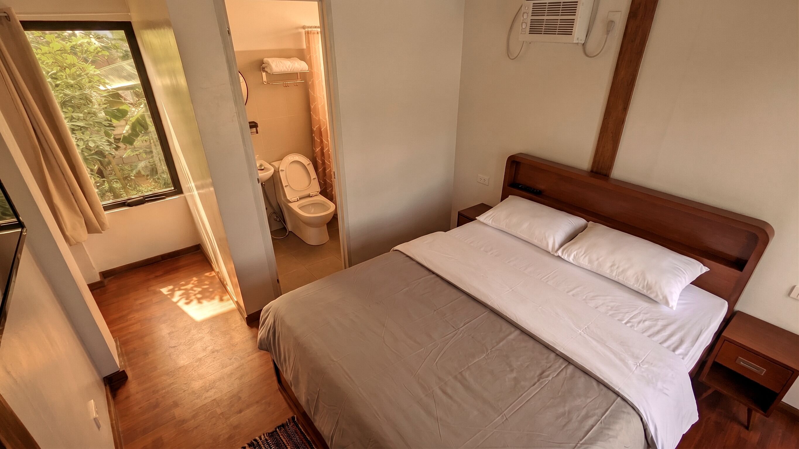 A bedroom with a wooden bed, a bedside table, and a view of the bathroom.