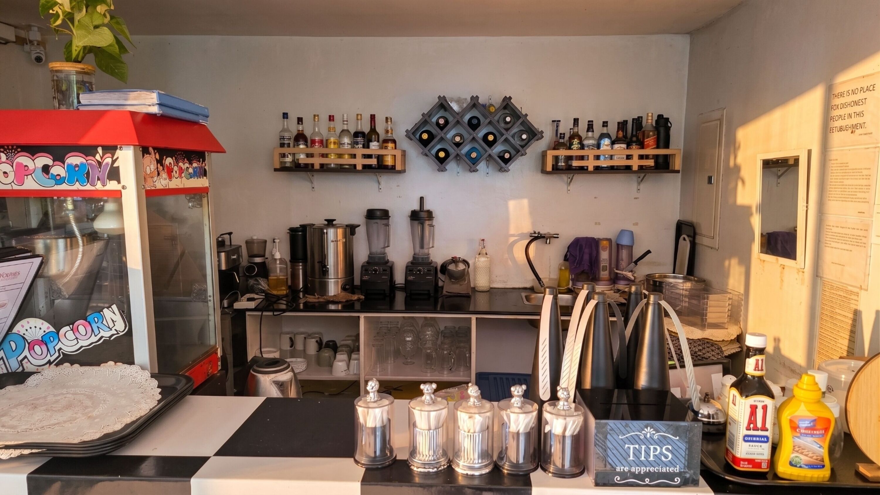 Zona de bar con máquina de palomitas, varias botellas de alcohol, una cafetera y un letrero que dice 'Se agradecen propinas'.