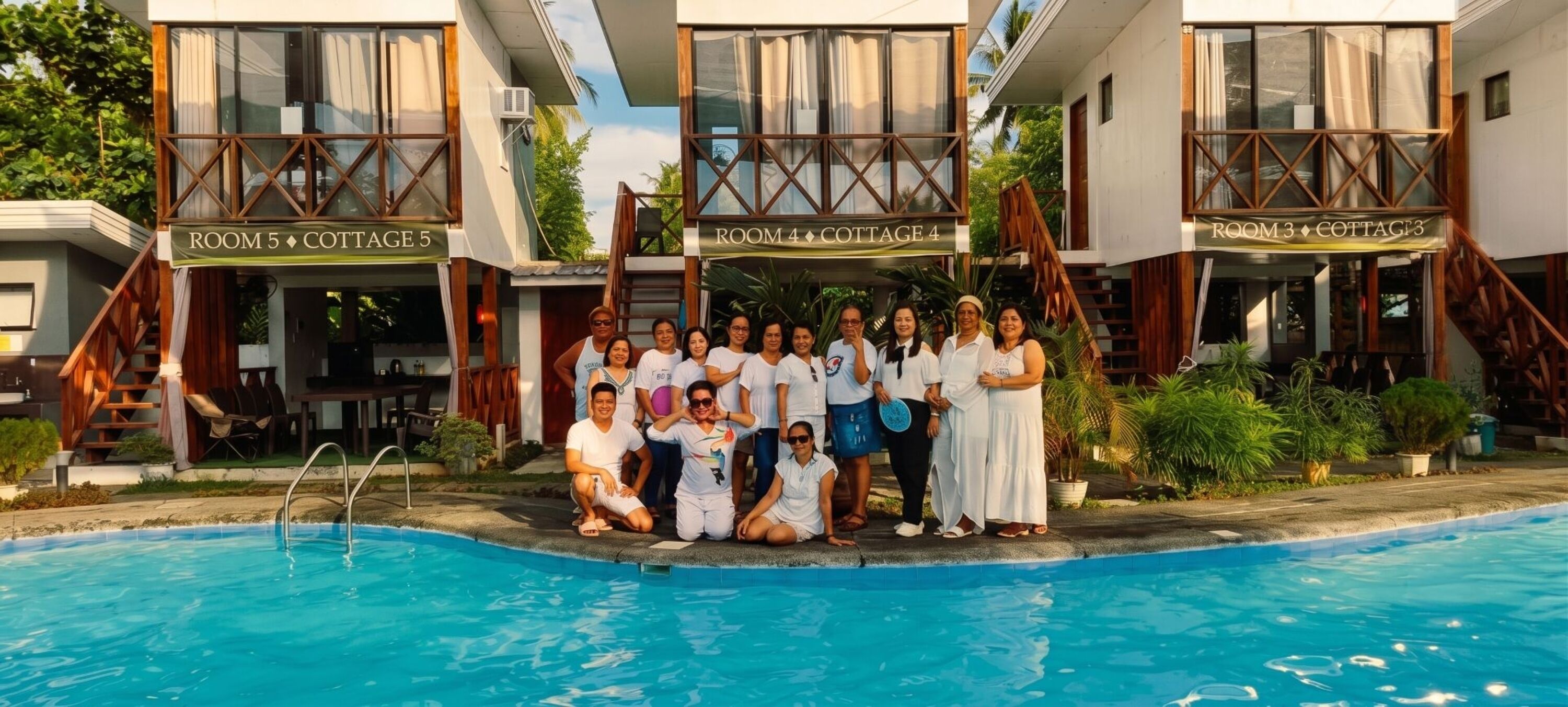 A group of people posing by a pool in a building with labeled rooms and a staircase.