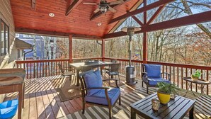 Eine überdachte Terrasse im Freien mit Holzboden, einem Tisch, Stühlen und einem Grill.