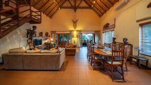 A spacious living room with a high ceiling, a dining area with wooden furniture, and a staircase leading to an upper level.
