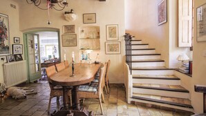 Un comedor con una mesa de madera, sillas de mimbre y una escalera que sube a otro nivel.