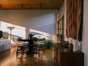 A modern interior with a dining area, a sofa, a lamp, and a large window allowing natural light. - Hygge Sunrise Lane Home (Lake Leelanau)