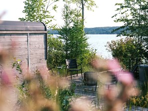A wooden deck with a metal barrel, a chair, and a bench overlooking a body of water.