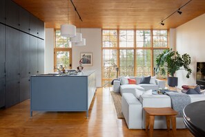 Eine moderne Küche mit Kochinsel, einem Essbereich inklusive Sofa und Tisch, sowie großen Fenstern für natürliches Licht.
