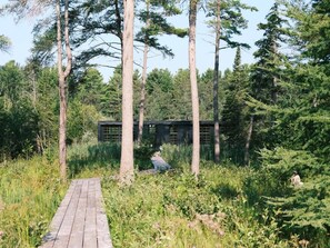 A wooden pathway leading to a cabin surrounded by tall trees. - Hygge Sunrise Lane Home (Lake Leelanau)