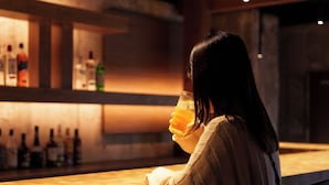 A person seated at a bar with a drink, with bottles in the background. - 3U NAMBA MINAMI - DOYANEN HOTELS (Osaka)