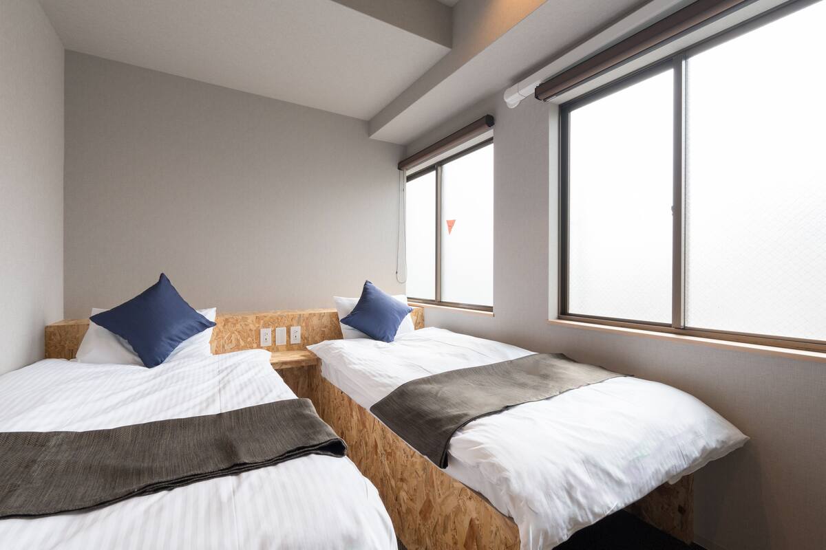 A hotel room with two beds, wooden headboards, white bedding, and large windows.