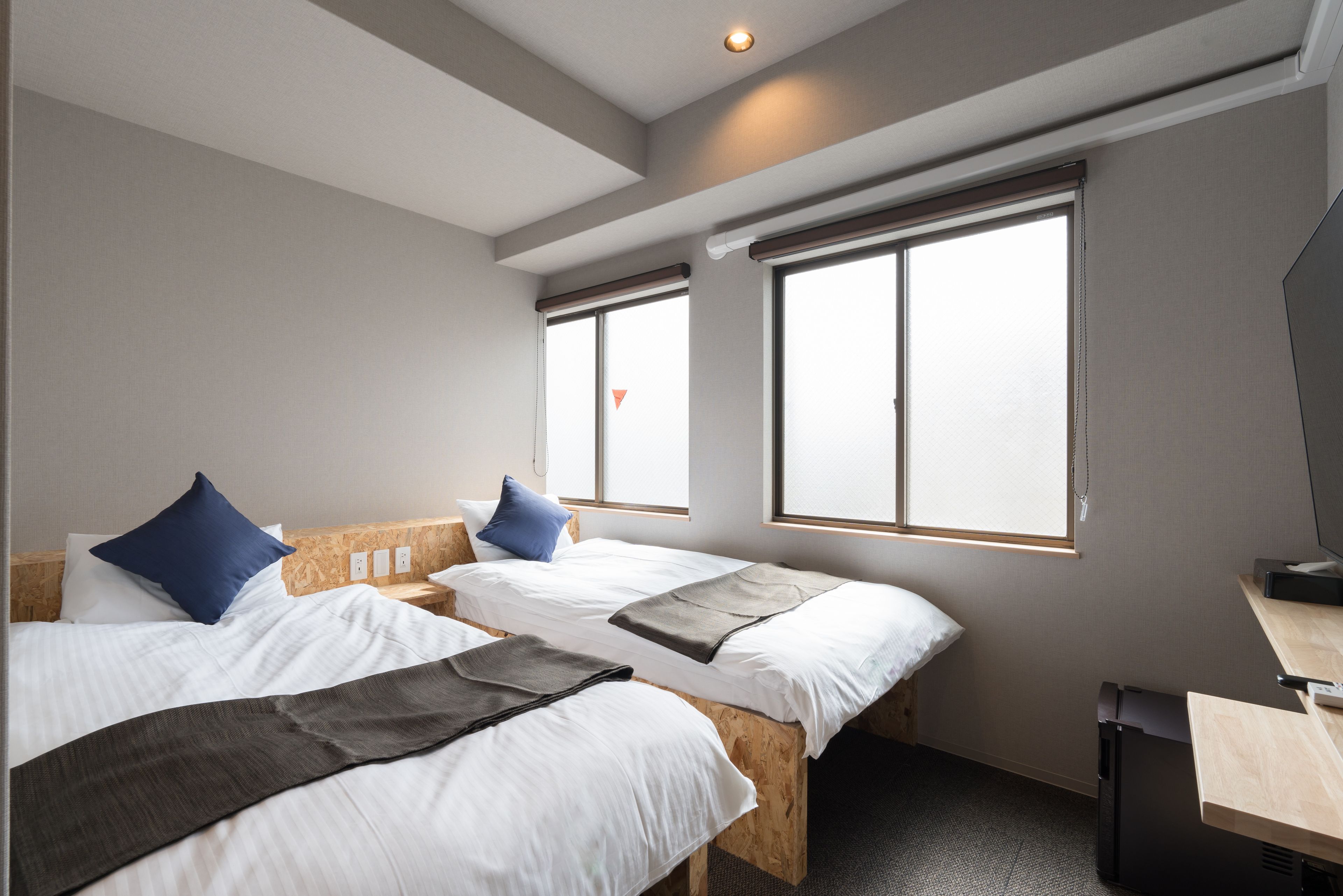 A hotel room with two beds, a desk, and large windows.