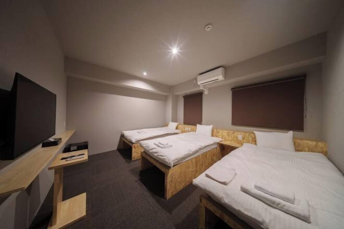 A hotel room with three single beds, a TV on a wooden stand, and an air conditioning unit on the wall.